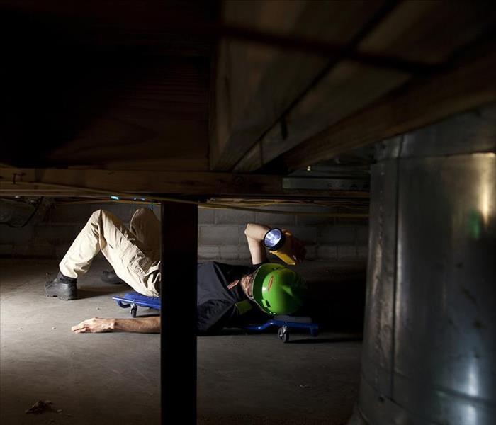 SERVPRO technician inspects crawlspace with flashlight.
