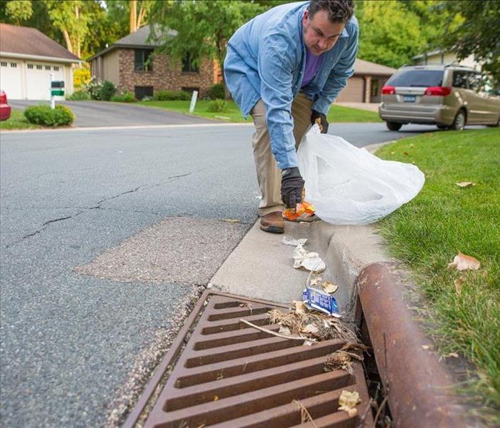 man clears trash from storm drain