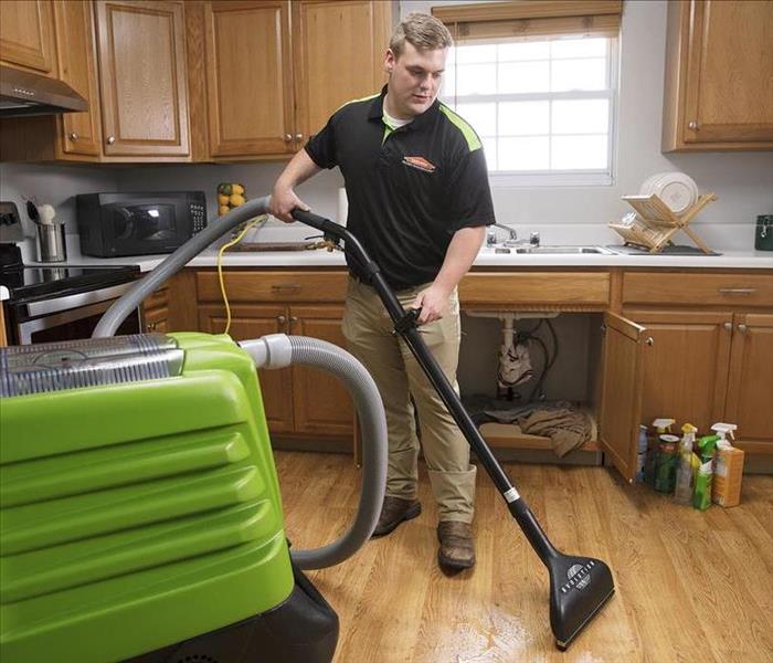 SERVPRO technician in a kitchen using a water extractor to remove water from the floor